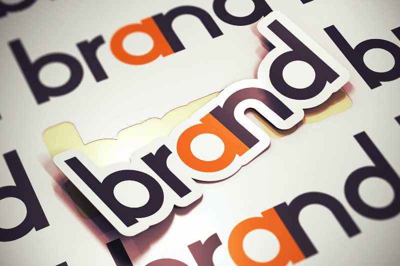 מיתוג חברות – מדבקות עם המילה brand בשחור והאות a בכתום על רקע של לוגו חוזר | מיתוג ועיצוב לוגו קרנף סטודיו